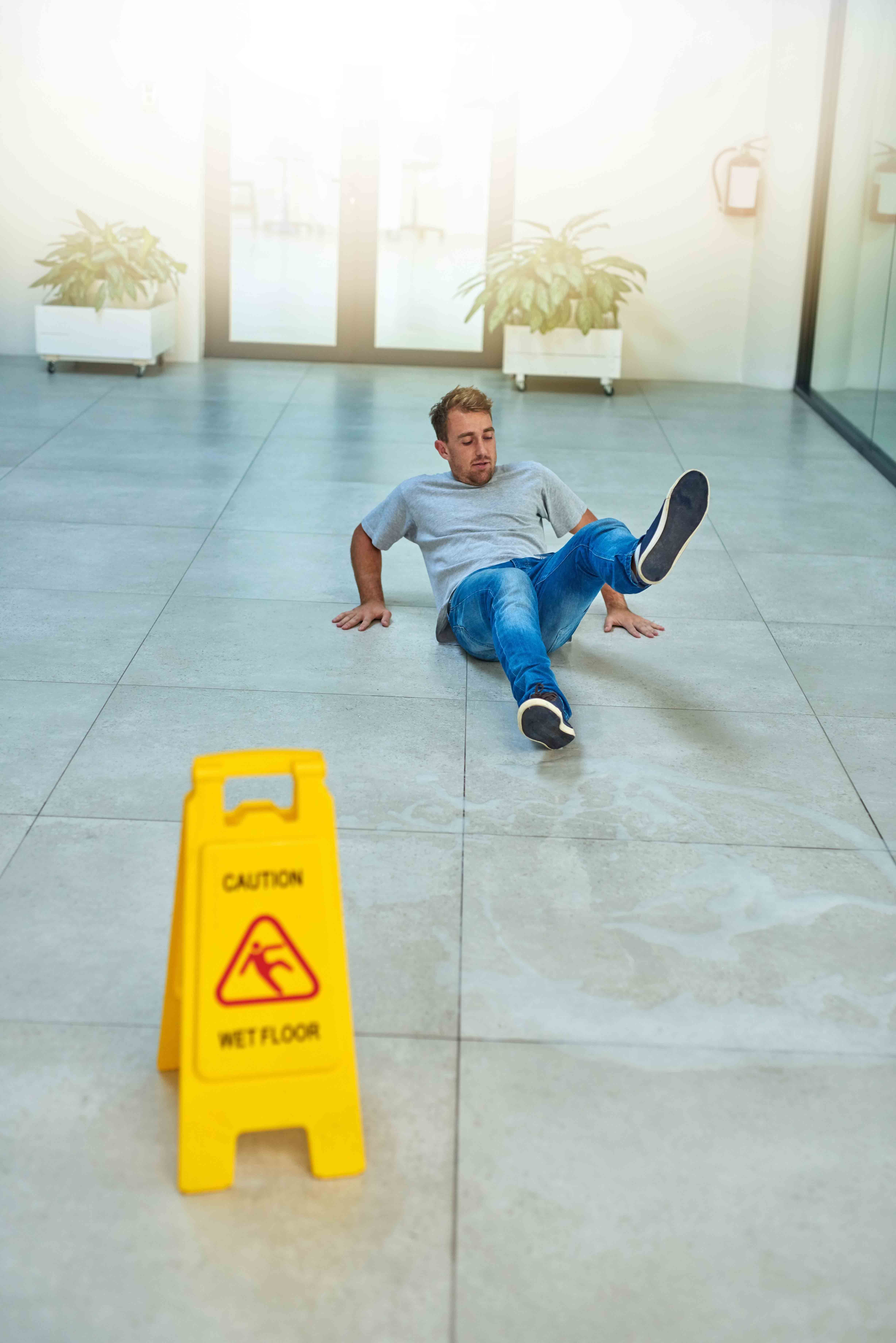 A man fallen on the floor near a wet floor sign, indicating a slip and fall accident.